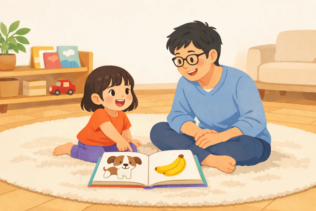 リビングの床で絵本を広げ、犬の絵を指さして声に出す幼児と、それを見守る父親